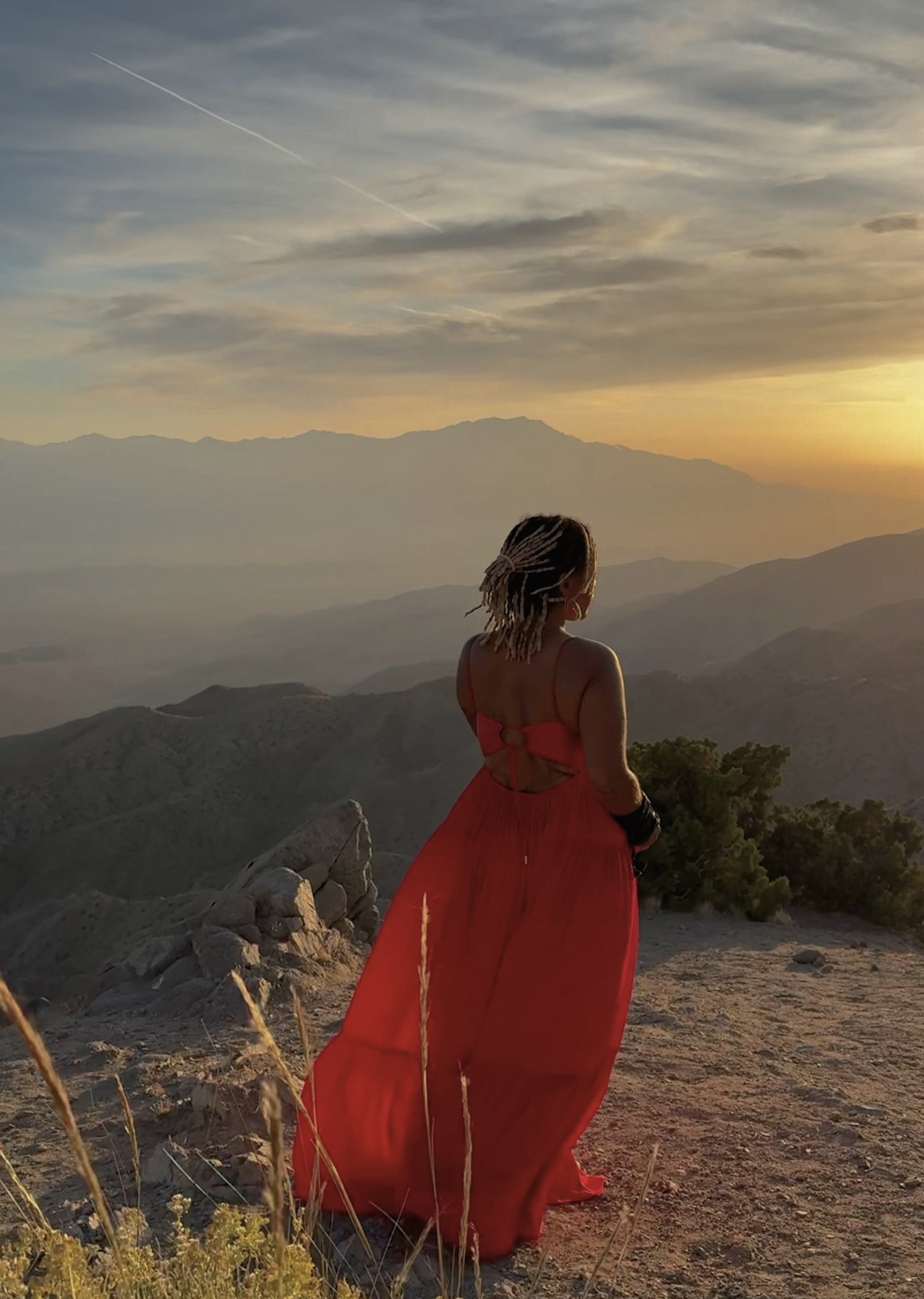 A woman in a red dress standing on a mountain overlook at golden hour